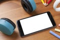 A blank screen smartphone on wooden table next to a pair of wireless earphones, some pencils and some chalks