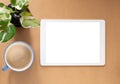 Blank screen of tablet and coffee cup with plant on brwon workplace.