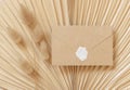 Blank sealed envelope on dry beige palm leaf near hare`s tail grass top view, boho wedding mockup