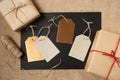 A blank sheet of black paper is surrounded by paper-wrapped gifts and gift tags on a canvas background. Copy space.