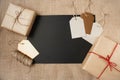 A blank sheet of black paper is surrounded by paper-wrapped gifts and gift tags on a canvas background.