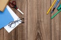 A blank sheet of paper, a notebook, pens, glasses, scissors on a wooden table top, space for text