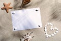 A blank sheet of white paper lies among various marine objects on the sandy surface of the beach