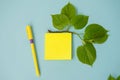 A blank sheet, a yellow sticker, a top view, a branch with leaves on a bright blue table with a pen