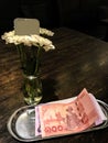 Blank signpost on flower glass vase and Thai Bank Notes one hundred Baht and five hundred Baht bank notes on silver tray