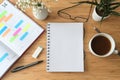 Blank spiral notebook mock-up on a wooden desk with organizer, coffee, glasses and flowers, copy space, flat lay