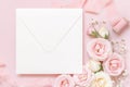 Blank square envelope between pink roses and pink silk ribbons on pink top view, wedding mockup