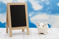 Blank standing chalkboard with a piggy bank on weathered wood with clear sky