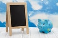 Blank standing chalkboard with a piggy bank on weathered wood with clear sky