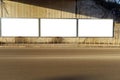 Blank street billboards on a grunge concrete wall in an underpass. Metal bollards, sidewalk and asphalt road in front.