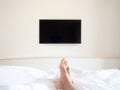 Blank television on white wall in front of the bed. first person view from bed seeing men feet and TV.