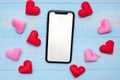 Blank touchscreen display of black smart phone with red and pink hearts shape decoration on blue wooden table background. Love,
