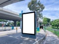 Blank vertical advertising poster banner mockup at empty bus stop shelter by main road, greenery behind. Out-of-home OOH vertical Royalty Free Stock Photo
