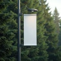 Blank vertical banner hangs from lamppost with blurred evergreen trees backdrop. White advertising board for message display. Royalty Free Stock Photo