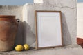 Blank vertical wooden frame picture mock up with vintage olive clay storage pot, vase. White old textured white wall in