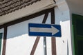 Blank white arrow on blue background street sign on pole with white wall with brown trim in background. Brown roof and green shutt Royalty Free Stock Photo