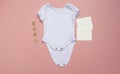 Blank white baby bodysuit grow mockup with `baby` letters and cream envelopes on a pastel pink background