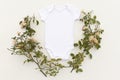 Blank white baby bodysuit surrounded by wild rose flowers