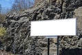 Blank white billboard on city street. In the background street and rocks. Mock up. Poster on street next to roadway. Empty space f