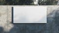 Blank white billboard mounted on a textured concrete wall with trees in the background, illuminated by soft natural Royalty Free Stock Photo