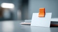 Blank white business card held by orange clip on reflective surface with blurred background and stack of cards Royalty Free Stock Photo