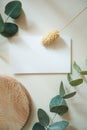 Blank white business greeting card mockup, fresh eucalyptus branches and dried flower on beige table backgound