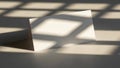 Blank white card casting a shadow with geometric light patterns on a neutral surface Royalty Free Stock Photo