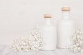 Blank white cosmetics bottles with small flowers on white wood board, mock up.