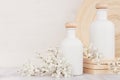 Blank white cosmetics bottles with small flowers on white wood board, copy space. Interior.