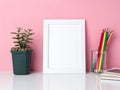 Blank white frame, crayon in jar, plant cactus on a white table