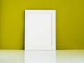 Blank white frame on a white table against the olive colored wall Royalty Free Stock Photo