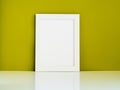 Blank white frame on a white table against the olive colored wall