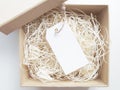 Blank white gift tag on shredded paper in a kraft box.