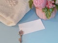 Blank white greeting card, silver key, bouquet of soap flowers and towel on blue background.