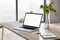 Blank white laptop monitor on wooden table with glass vase and notebook in sunny home office. 3D rendering, mock up