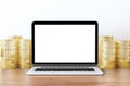 Blank white laptop screen with piles ofcoins on wooden table