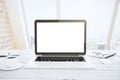 Blank white laptop screen on white wooden table with eyeglasses