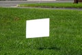 Blank white lawn sign on metal spikes on green grass near a sidewalk and street