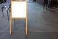 Blank white mockup template of an easel with a wooden frame on a pedestrian sidewalk. Royalty Free Stock Photo