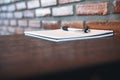 A blank white notebook and silver color pen on wooden table with brick wall Royalty Free Stock Photo