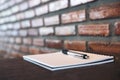 A blank white notebook and silver color pen on wooden table with brick wall Royalty Free Stock Photo