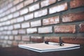 A blank white notebook and silver color pen on wooden table with brick wall Royalty Free Stock Photo