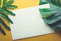 Blank white notepaper with tropical leaves laying on yellow table Royalty Free Stock Photo