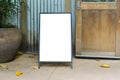Blank white outdoor advertising stand or sandwich board mockup template. Clear street signage board placed by a pot of plants.