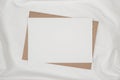 Blank white paper on brown paper envelope on white cloth. Mock-up of horizontal blank greeting card. Top view of Craft envelope on