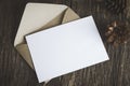 Blank white paper card with brown envelop and pine cones on old wooden table with vintage tone