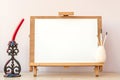 Blank white paper for painting on wooden easel, brushes and candle on table at home studio Royalty Free Stock Photo