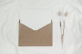 Blank white paper is placed on the open brown paper envelope with Rabbit tail dry flower on white cloth. Mock-up of horizontal Royalty Free Stock Photo