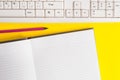 Blank white paper for textual messages. Copy space on notebook above yellow background with pc keyboard and pencil on