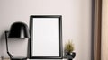 A blank white photo frame mockup with a lamp and small plant on the table, A minimal simple tone of photo frame look